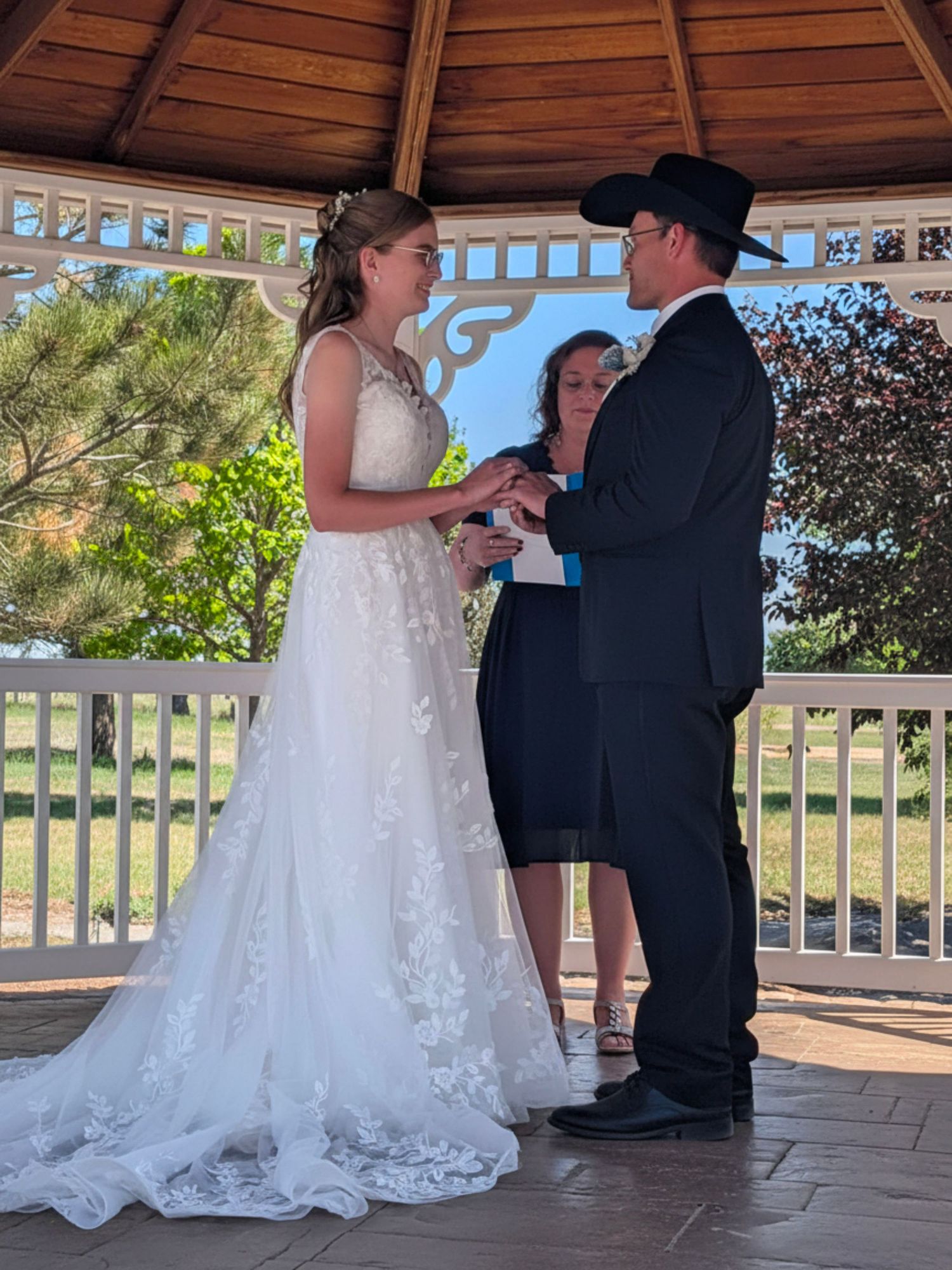 Bride and groom exchanging rings at outdoor gazebo wedding ceremony with officiant.