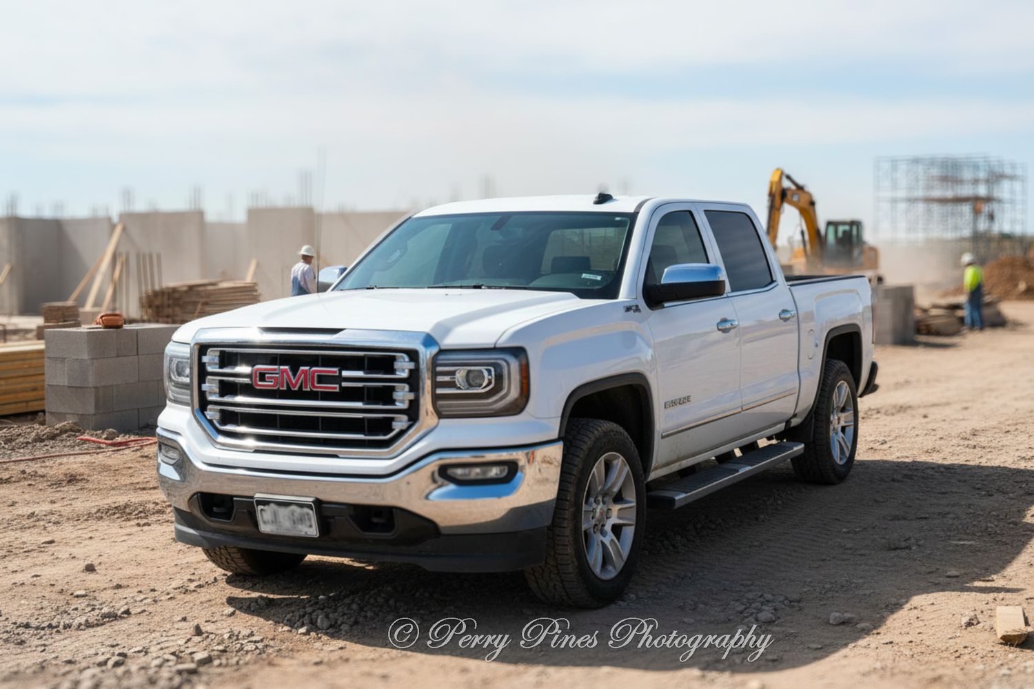 White GMC Sierra pickup truck parked at an active construction site with an excavator working in the background.