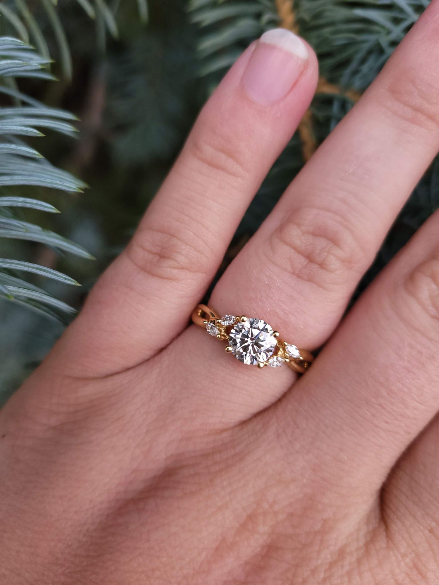 Close-up of elegant gold diamond solitaire engagement ring on finger with pine tree background.