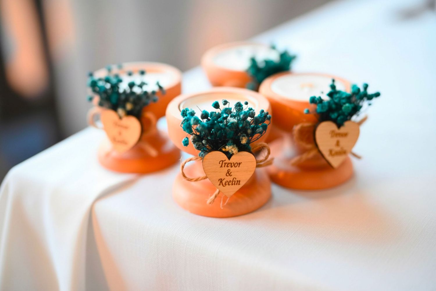 Orange terracotta pot wedding favors with teal flowers and personalized wooden heart tags.