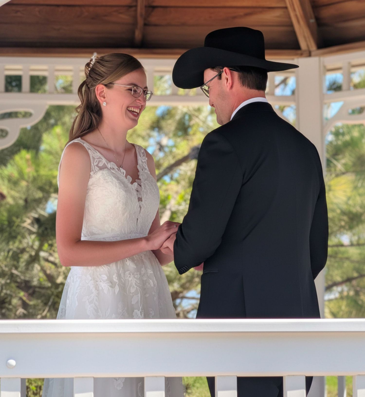Bride and groom exchanging vows under gazebo, groom wearing black cowboy hat.