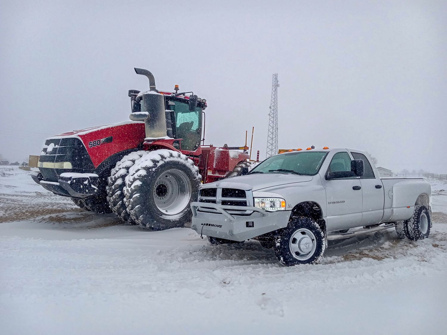 White Dodge Ram pickup truck parked beside a large red Case IH articulated tractor in snowy winter conditions.