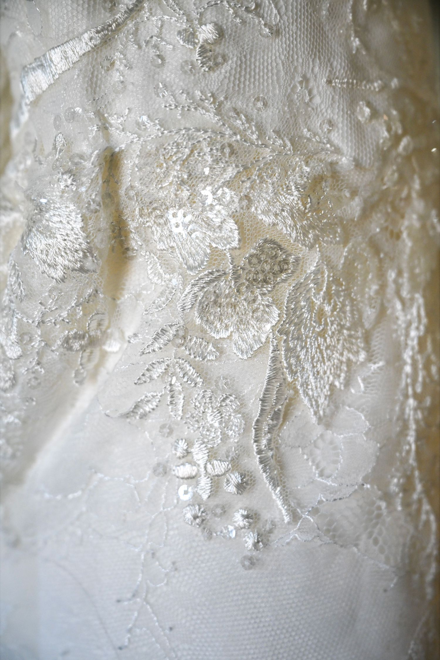 Close-up detail of intricate floral embroidery and beading on a white lace wedding gown.