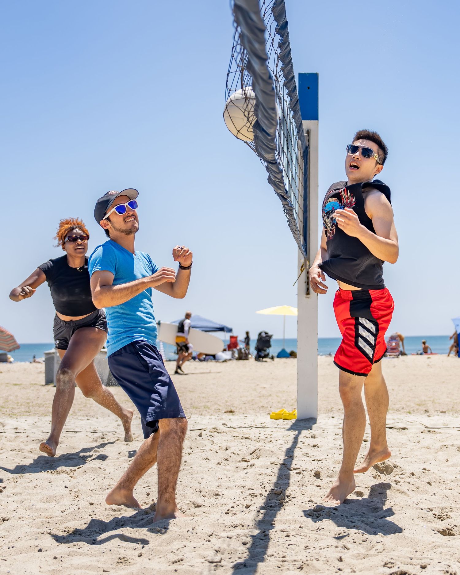 Group of friends playing beach volleyball near ocean on clear day.