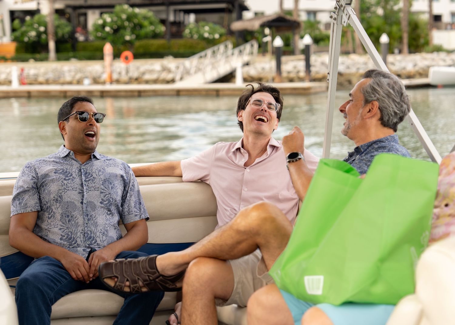 Three men laughing and relaxing together on a pontoon boat at a marina.