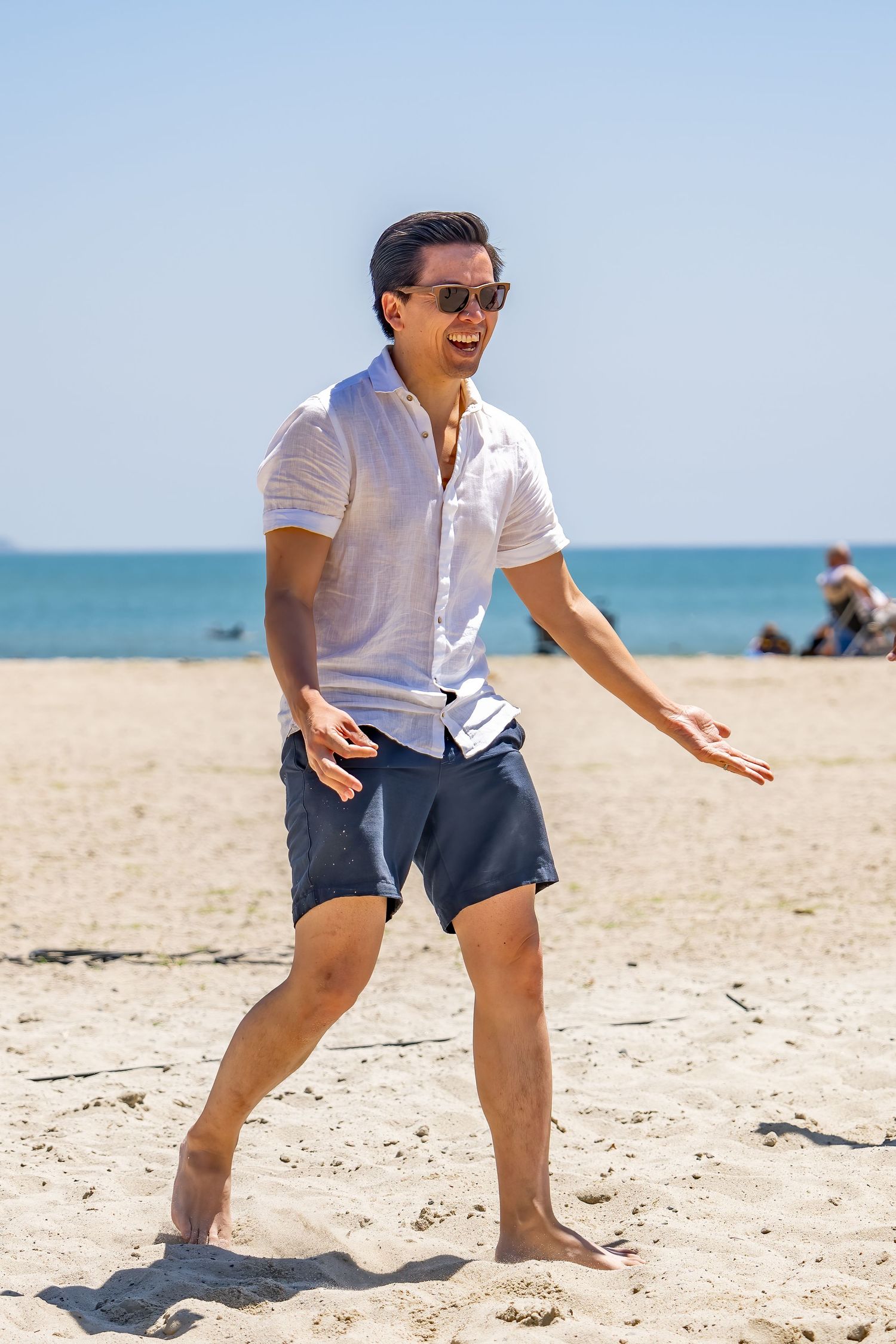 Man in white shirt and sunglasses playing beach volleyball on a sunny sandy beach.