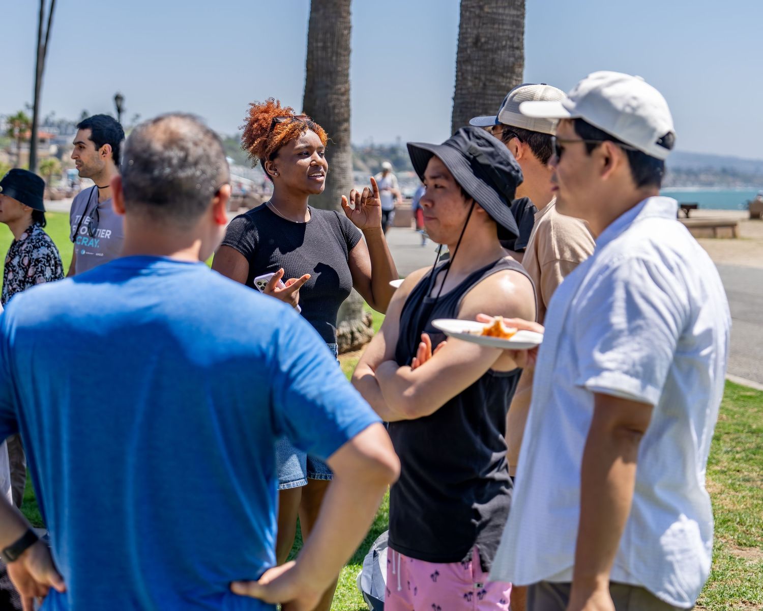 Diverse group of people talking and eating at a sunny outdoor beach park social gathering.