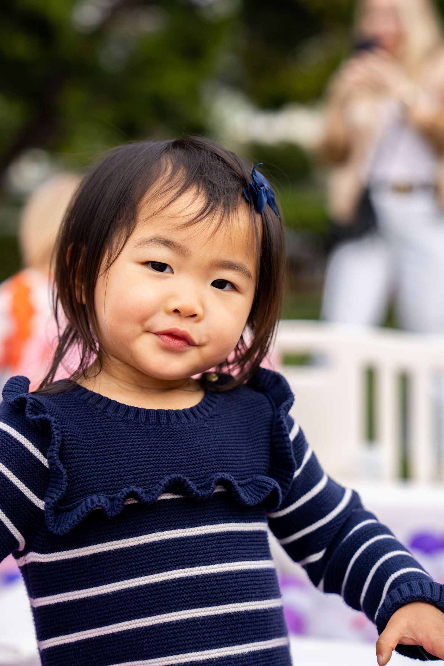 Adorable Asian toddler girl in navy striped dress smiling at an outdoor party.