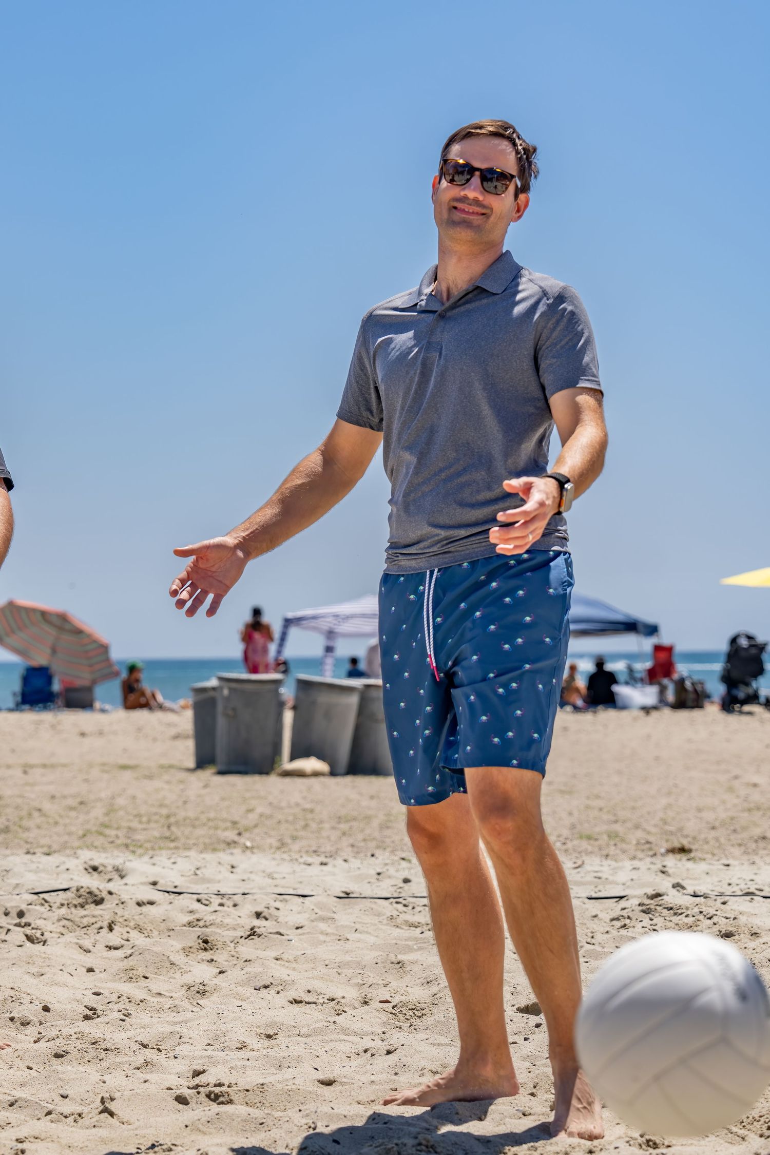 A man in blue shorts and sunglasses plays beach volleyball on a sunny day.