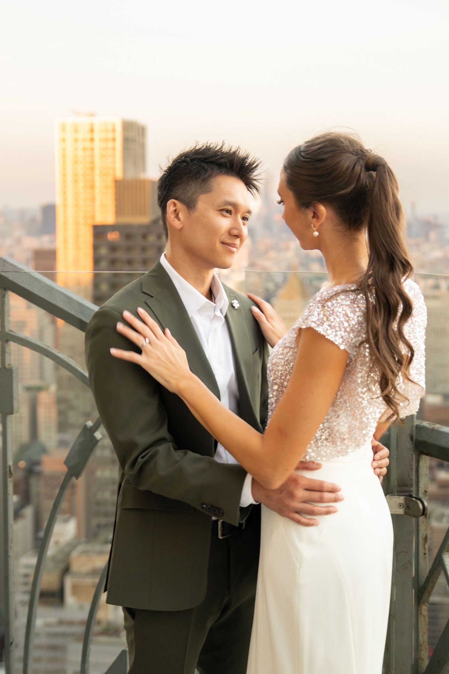 Bride and groom embracing on a rooftop terrace with a golden city skyline backdrop.
