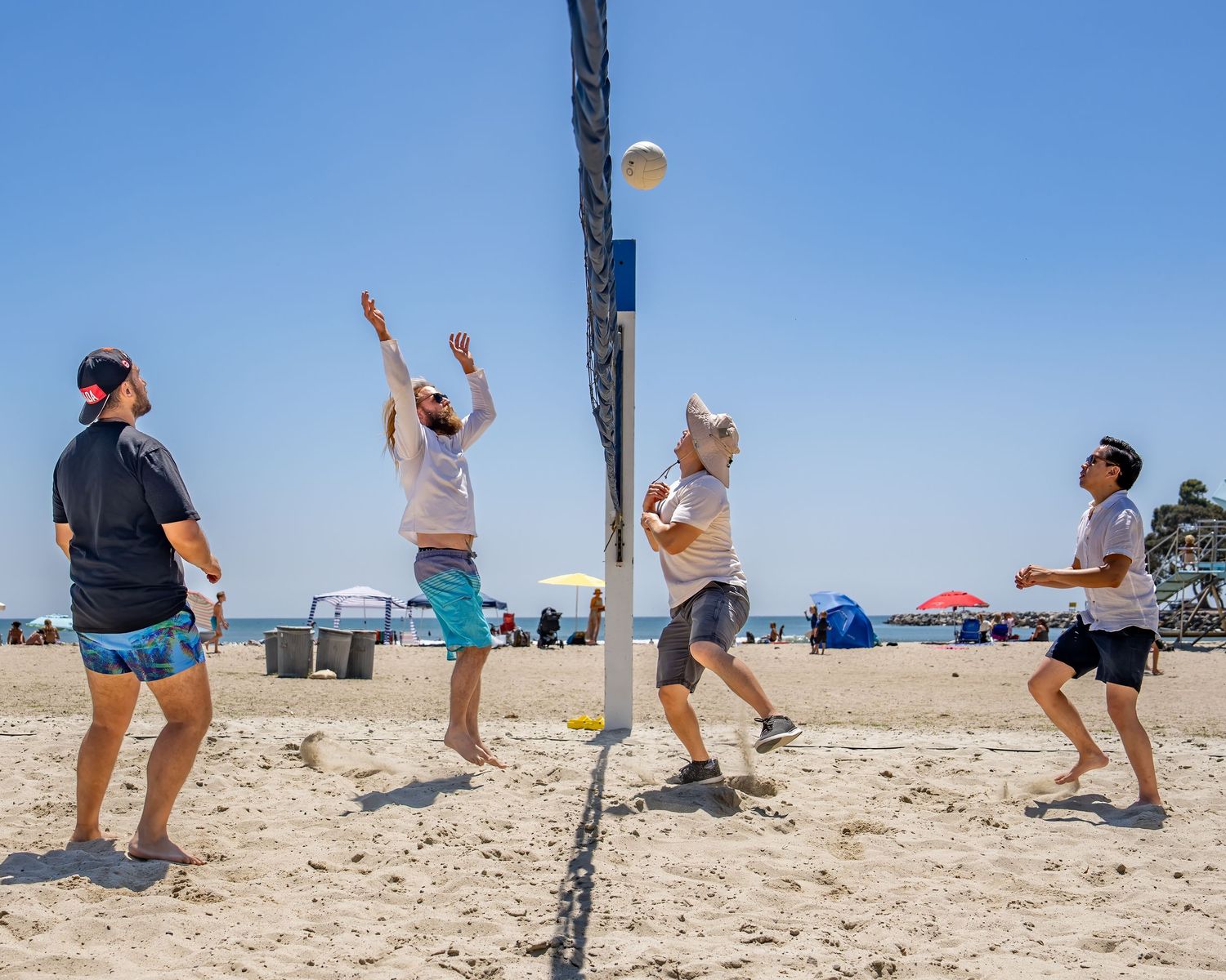 Four players compete in beach volleyball game at sunny seaside court.