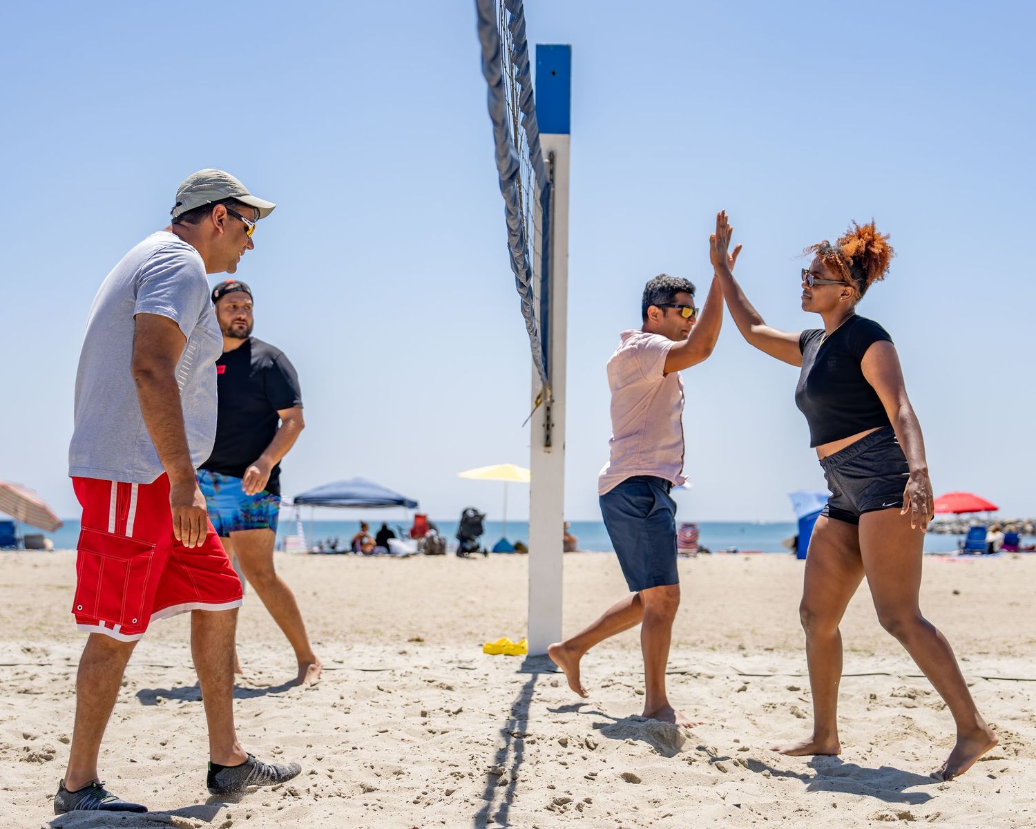 Two beach volleyball players high-fiving near the net on a sunny sandy beach.