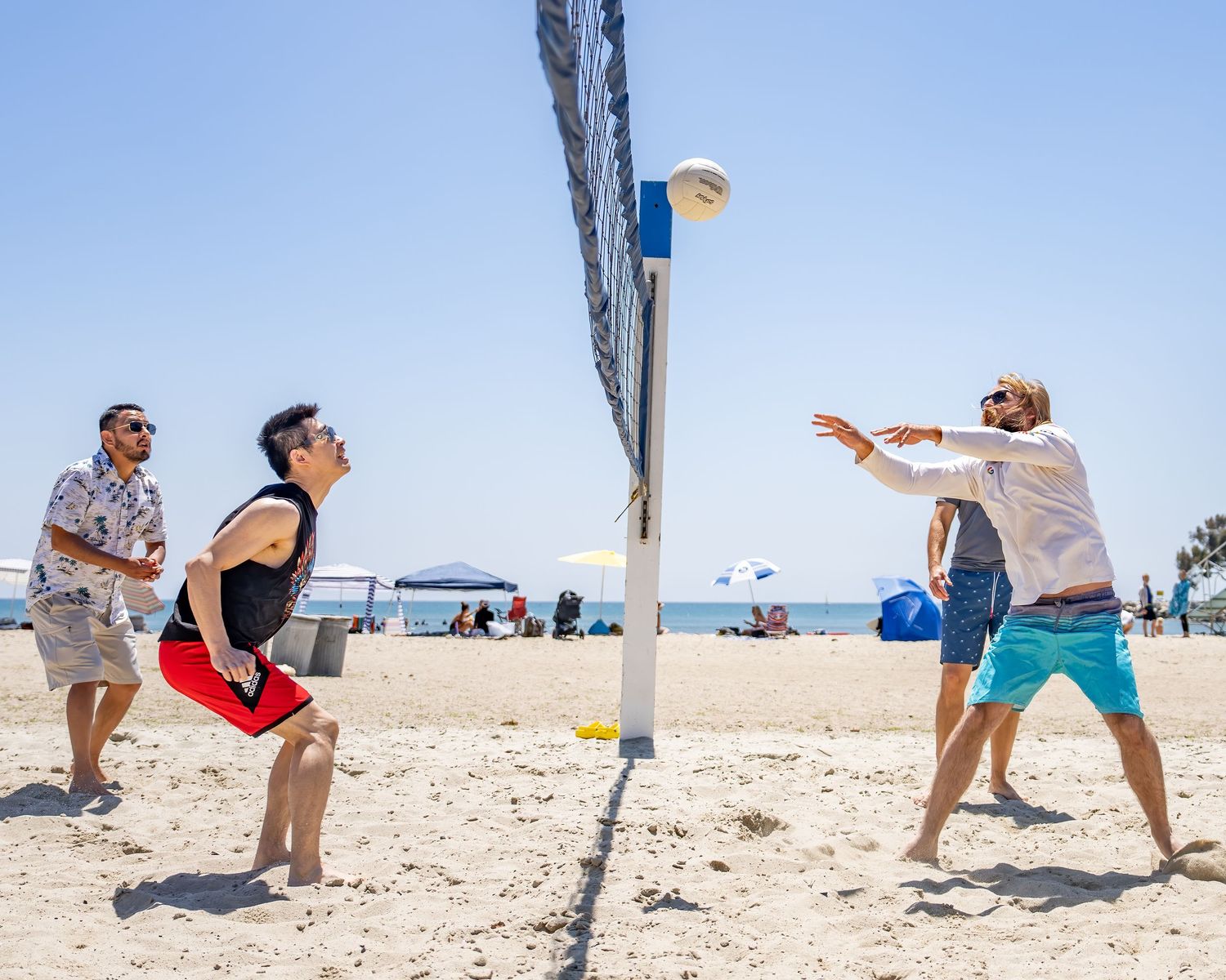 Three people playing beach volleyball near a net on a bright sunny day.