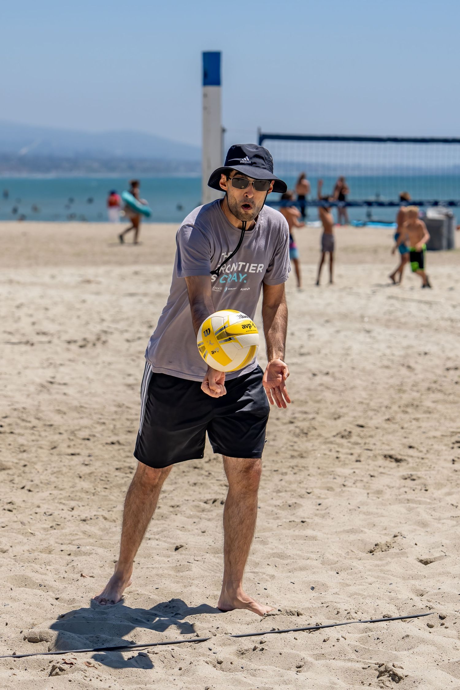 Man in bucket hat playing beach volleyball, preparing to bump the ball on a sunny sandy beach.