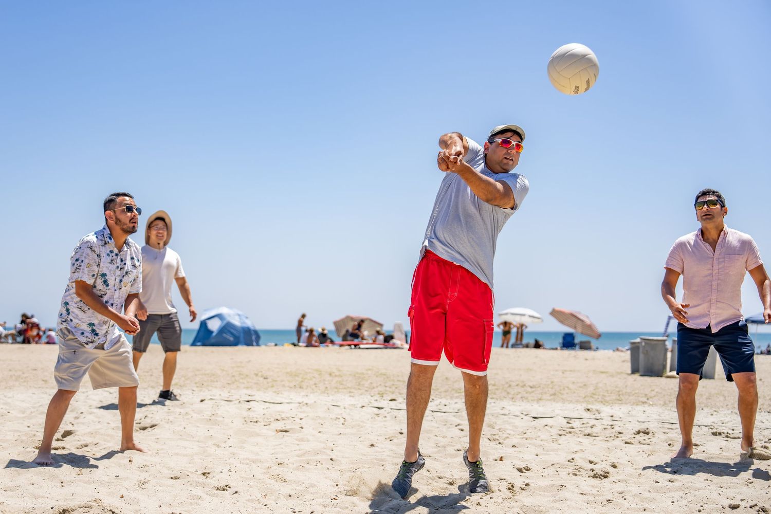 Group of four people playing beach volleyball on a sunny sandy beach.
