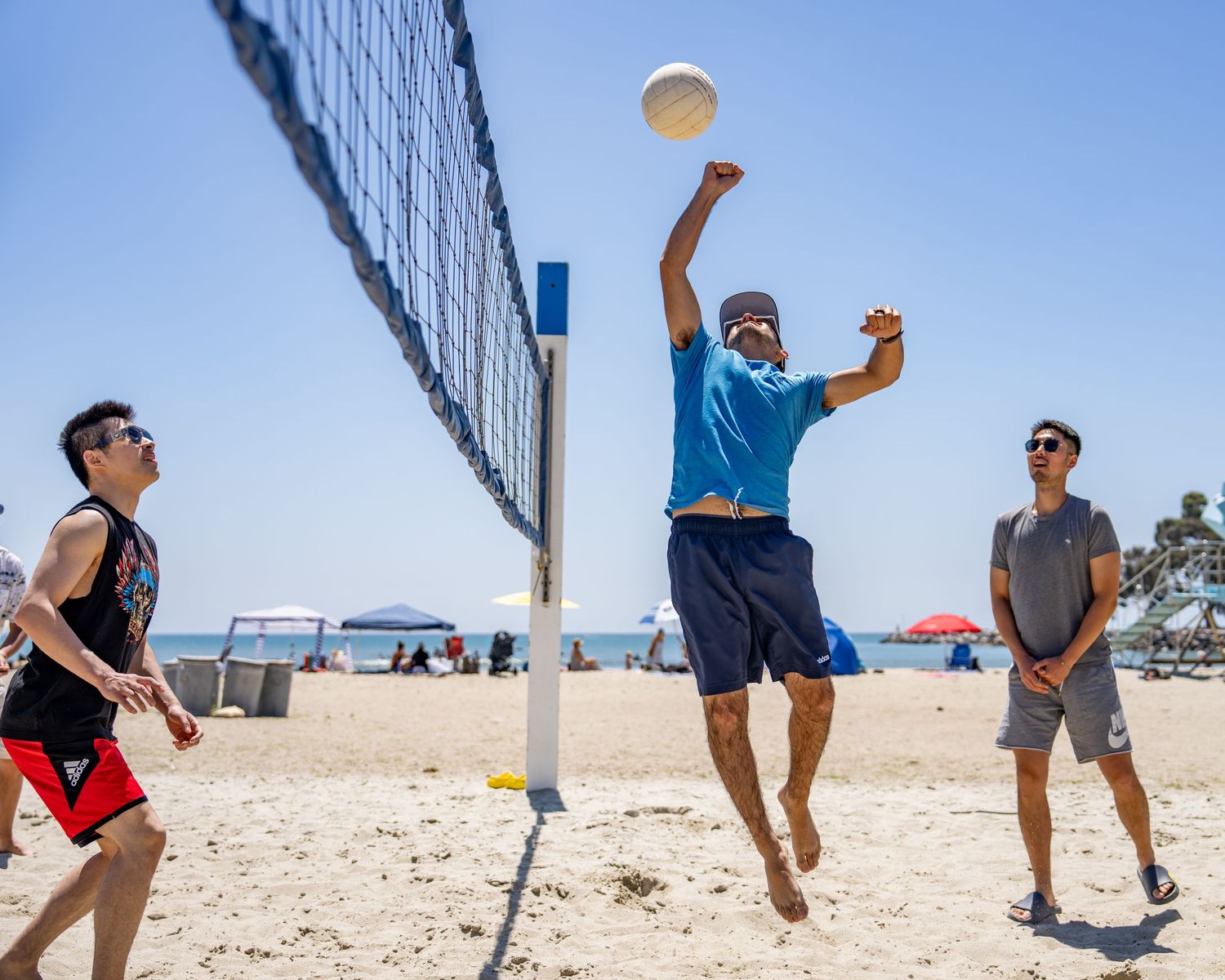 Three men playing beach volleyball near the net on a sunny sandy beach.