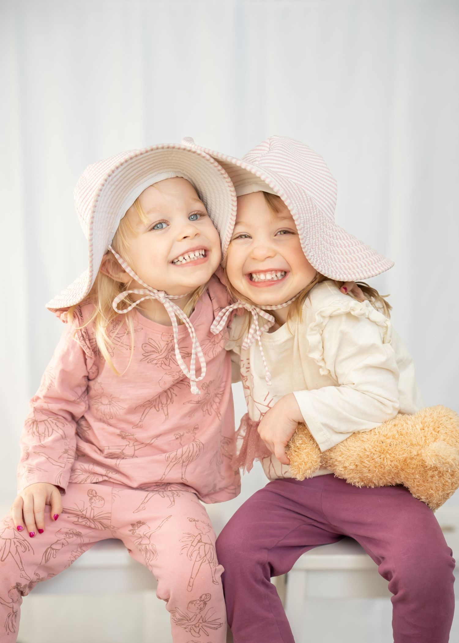 Two smiling little girls wearing pink sun hats posing together against white background.