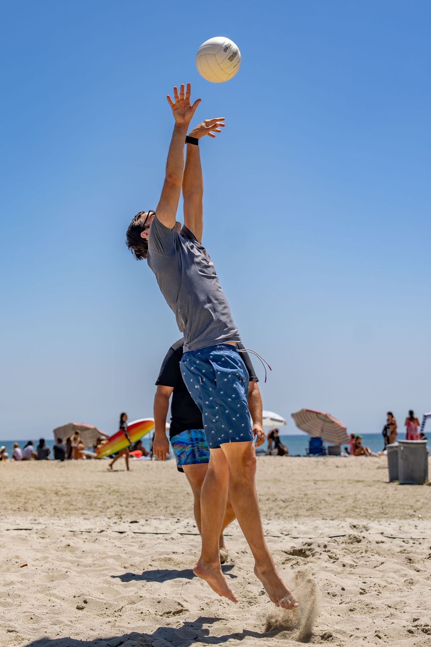 A man jumps to spike a volleyball on a crowded sunny beach.