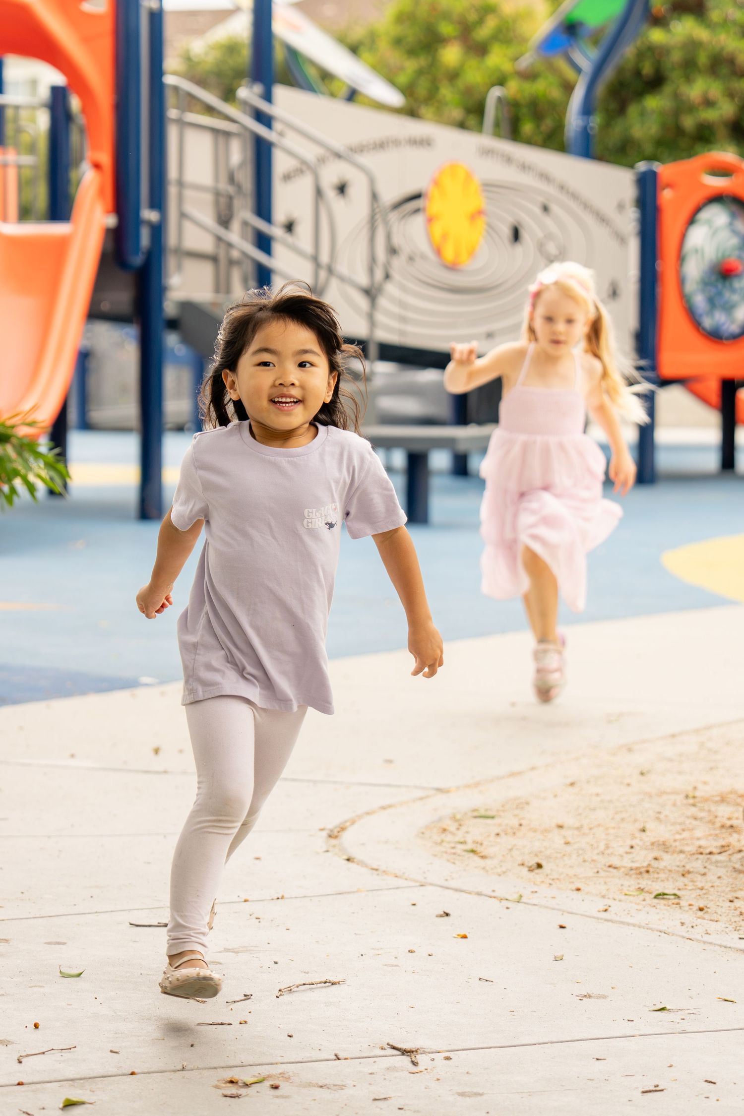 Two young girls running and playing on a colorful outdoor playground on a sunny day.