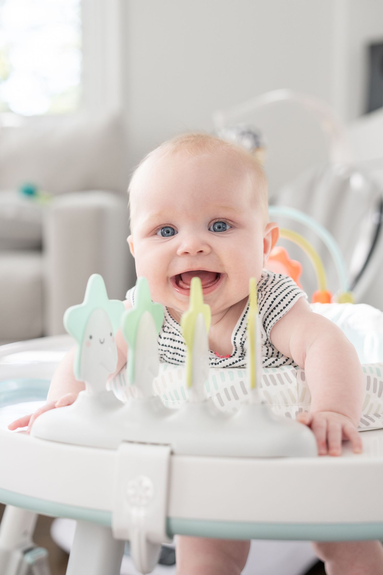 A happy baby with blue eyes sits in a play activity center smiling.