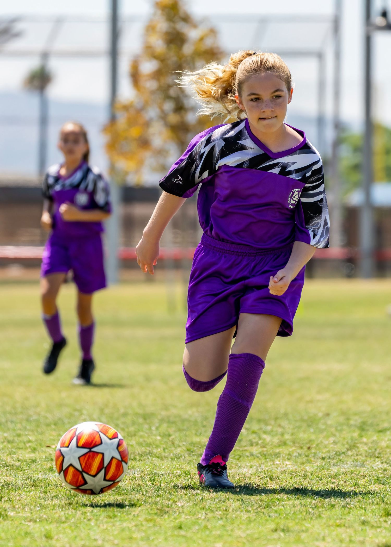 Young girl in purple soccer uniform dribbling ball during outdoor youth soccer game.