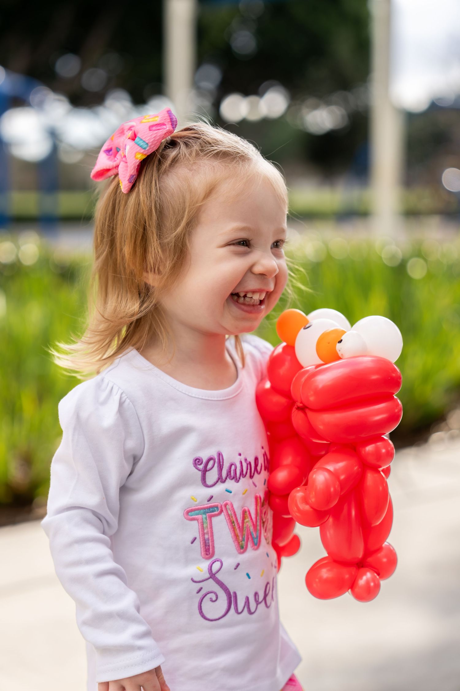 Happy little girl laughing while holding a red Elmo balloon animal at an outdoor party.