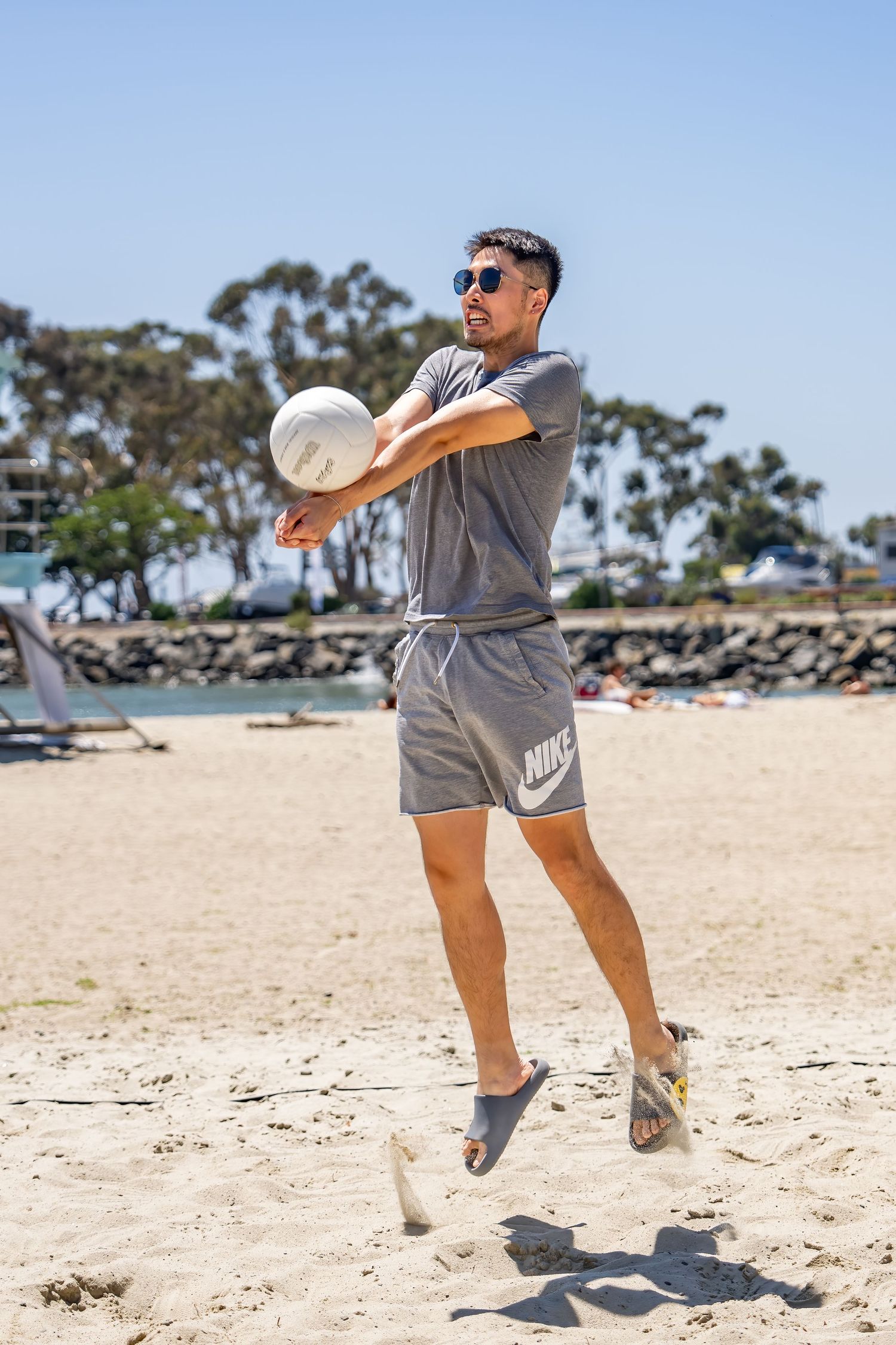 Man in gray Nike outfit jumping to hit a volleyball on a sandy beach.