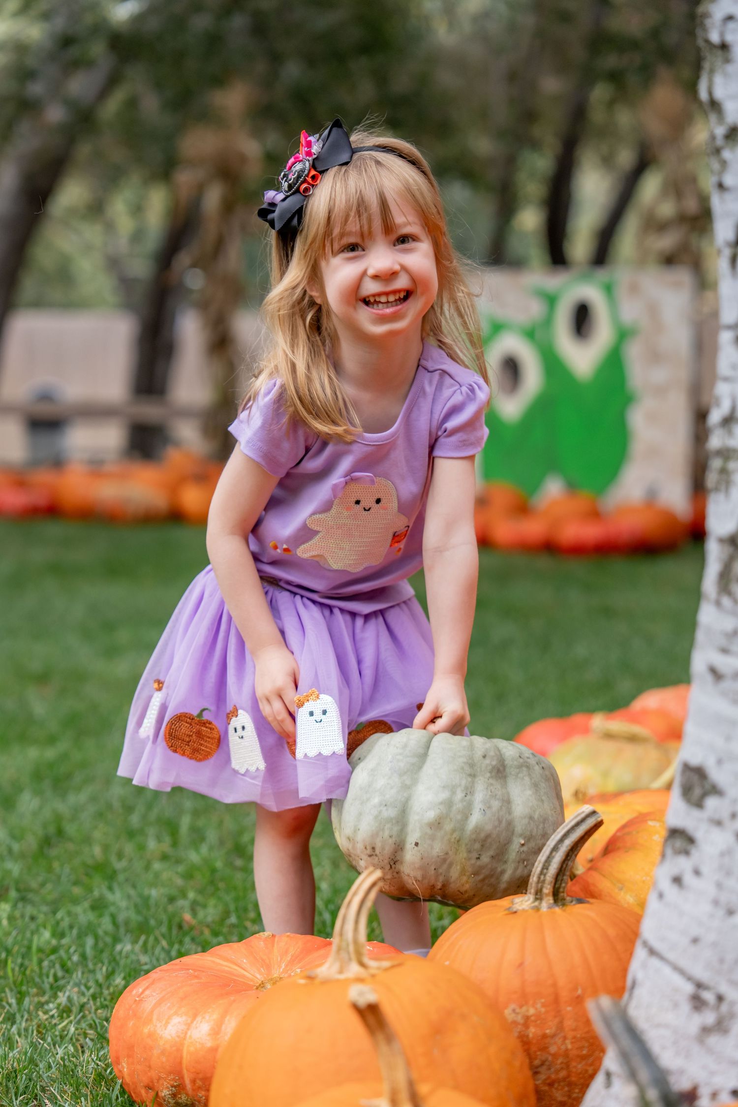 Laughing little girl in purple ghost dress posing with pumpkins at Halloween patch.