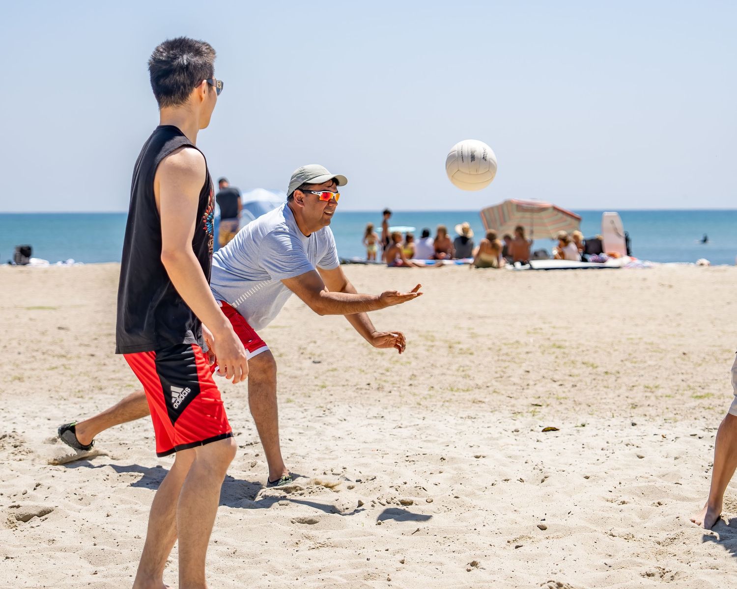 Two men playing beach volleyball on a sunny day with a ball in the air.