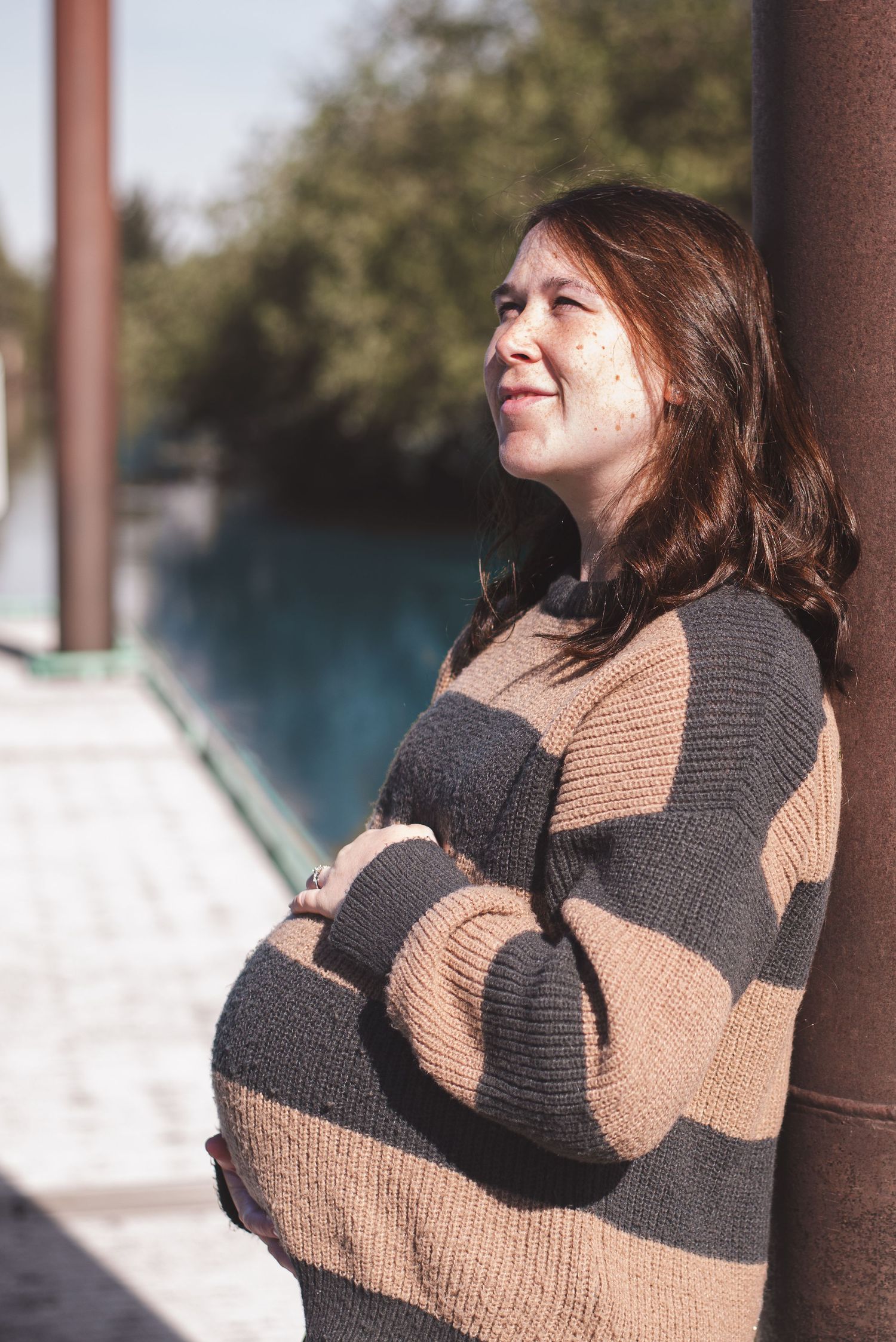 A photo of a pregnant woman leaning against a metal pole.