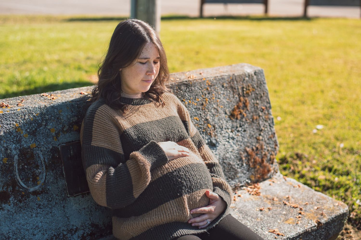 A photo of a pregnant woman sitting on a bench.