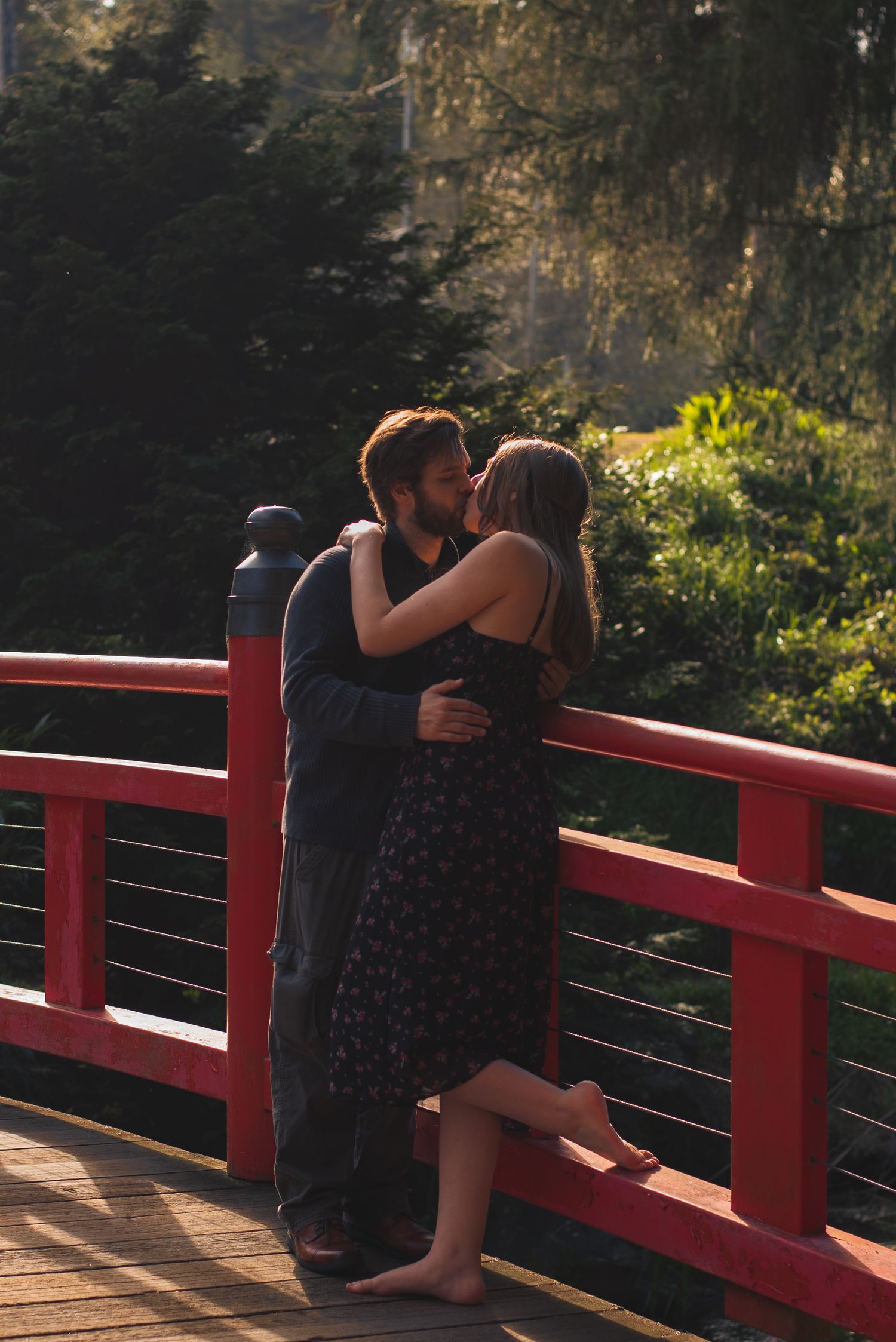 A photo of a couple kissing on a bridge.