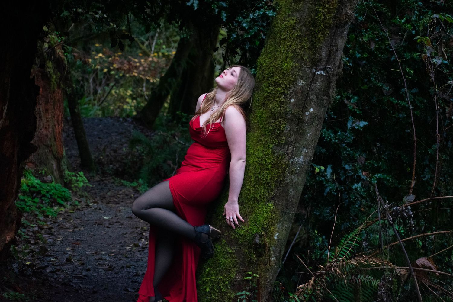 A photo of a woman leaning against a tree.