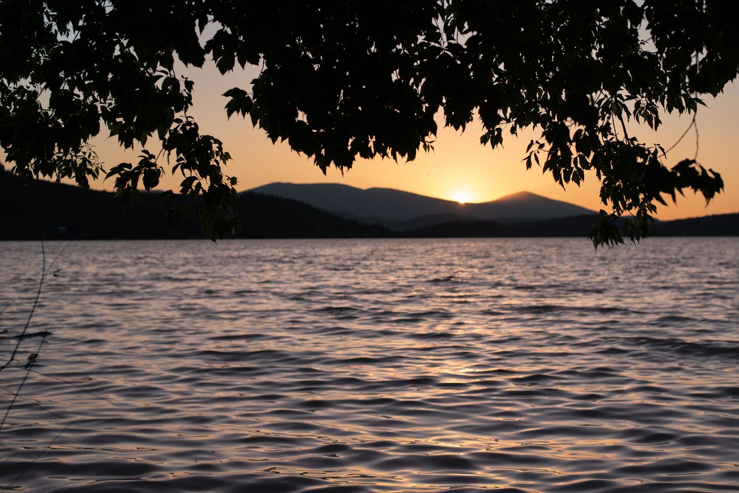 A photo of a body of water with mountains in background during a sunset.