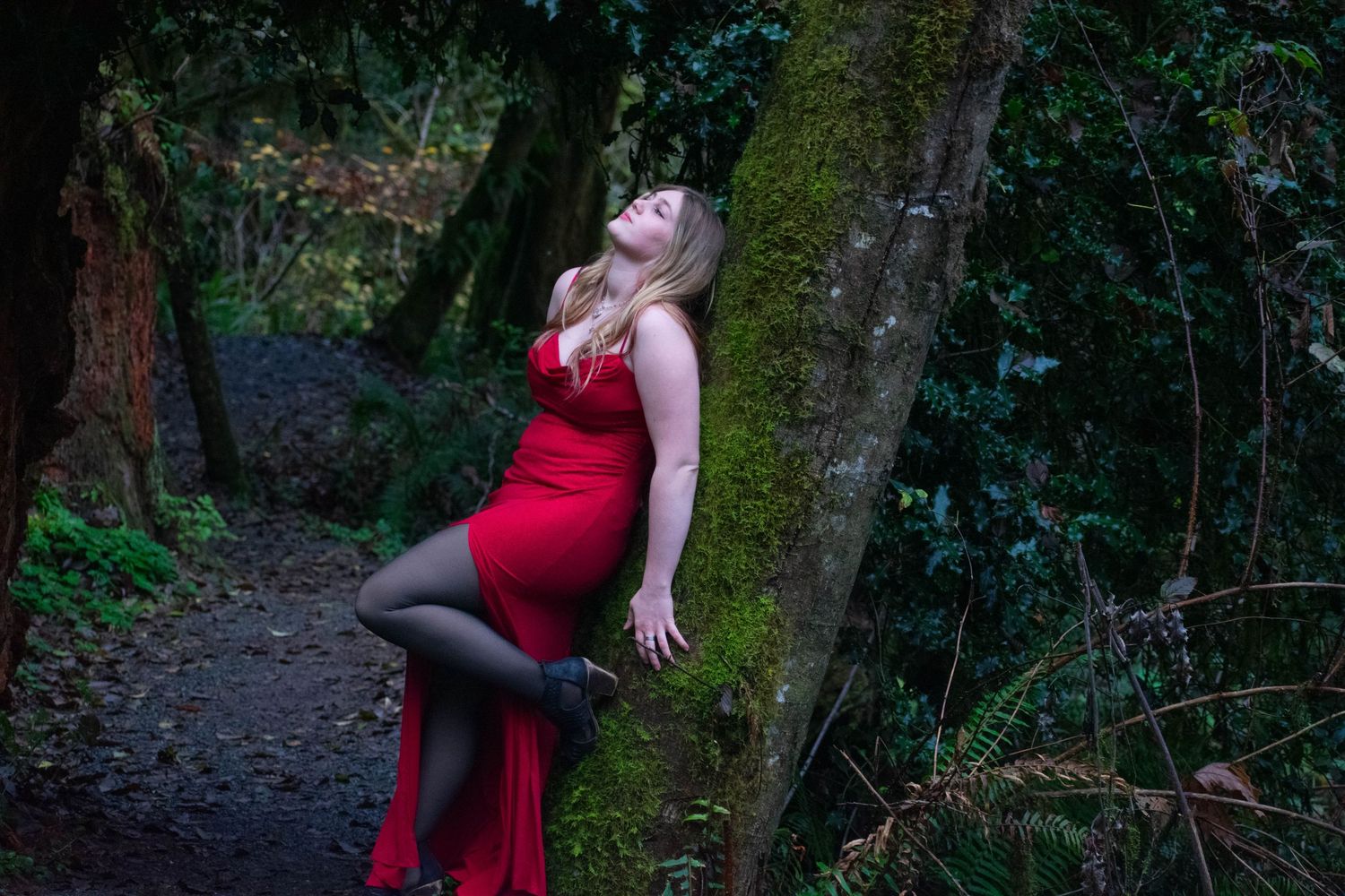 A photo of a woman leaning against a tree.