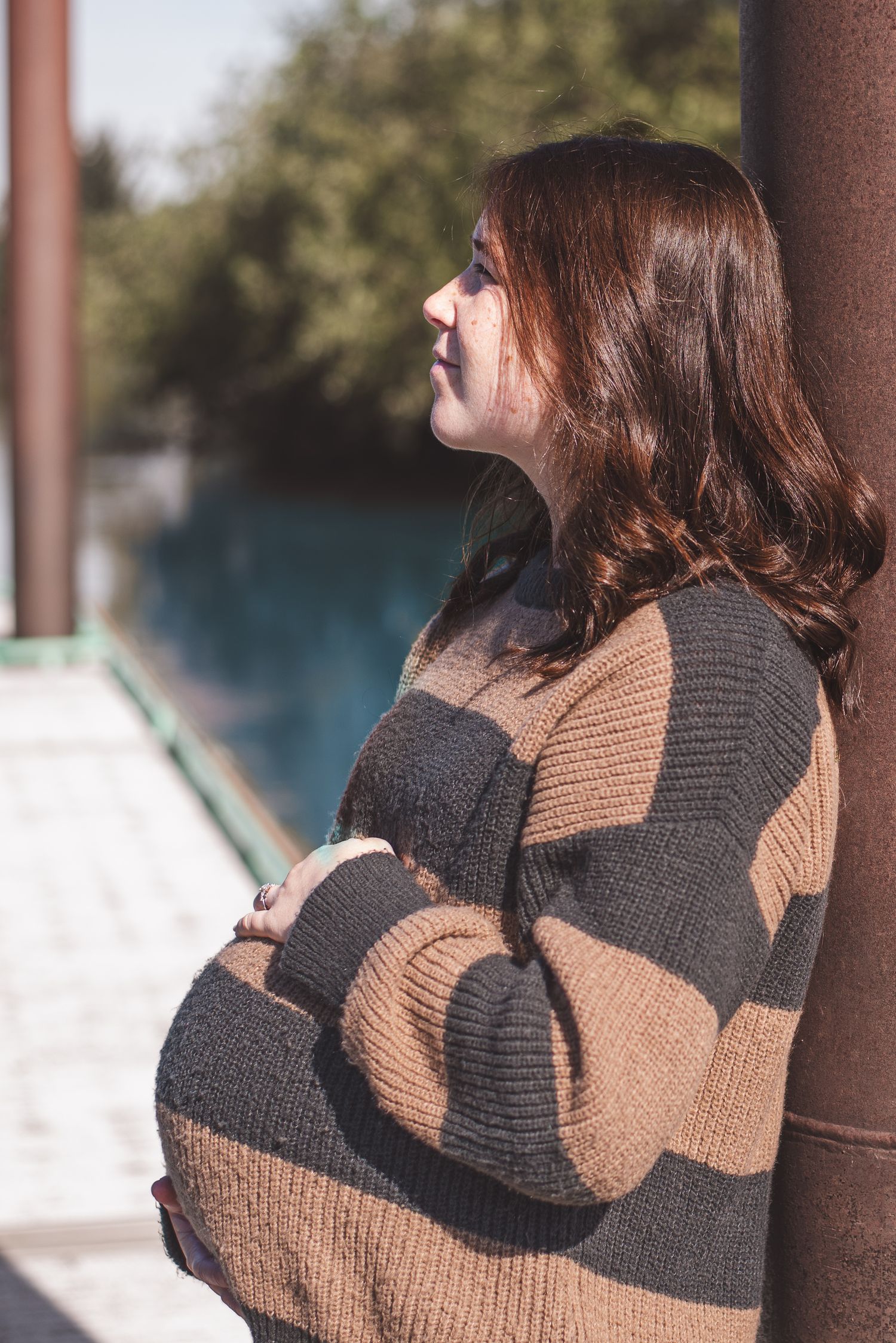 A photo of a pregnant woman leaning against a metal pole.
