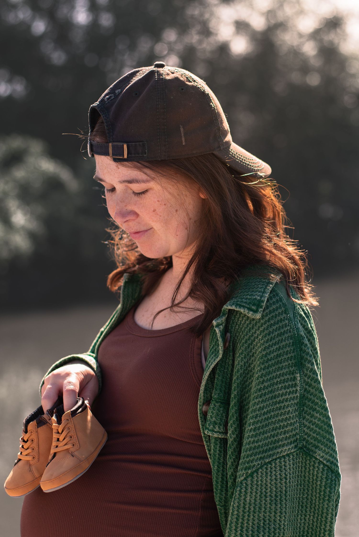 A photo of a pregnant woman holding baby shoes to her stomach.