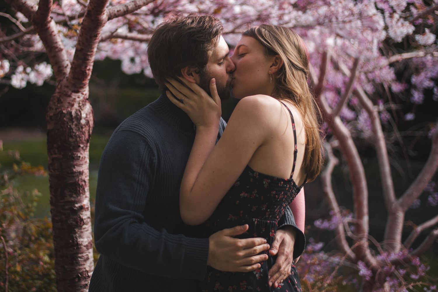A photo of a couple kissing in front of trees.