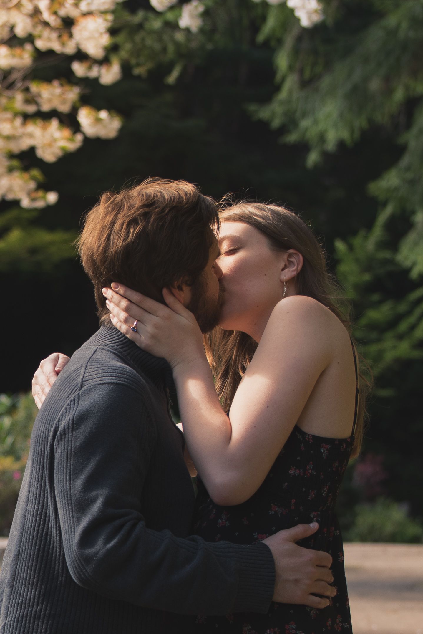 A photo of a couple kissing in front of trees.