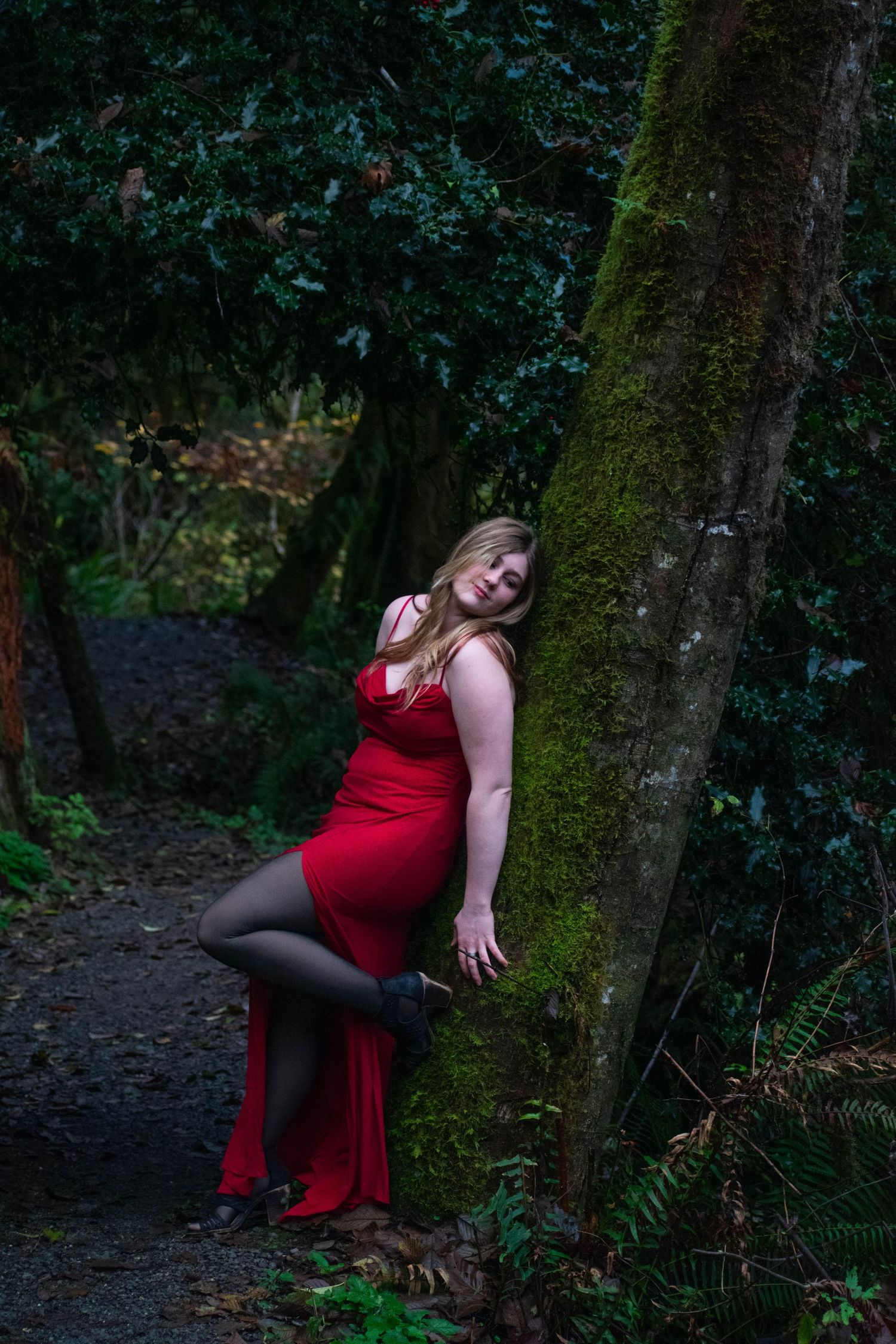 A photo of a woman leaning against a tree.