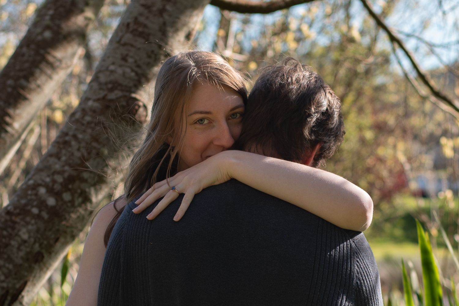 A photo of an engaged couple hugging with the woman peeking out over her fiancé's shoulder.