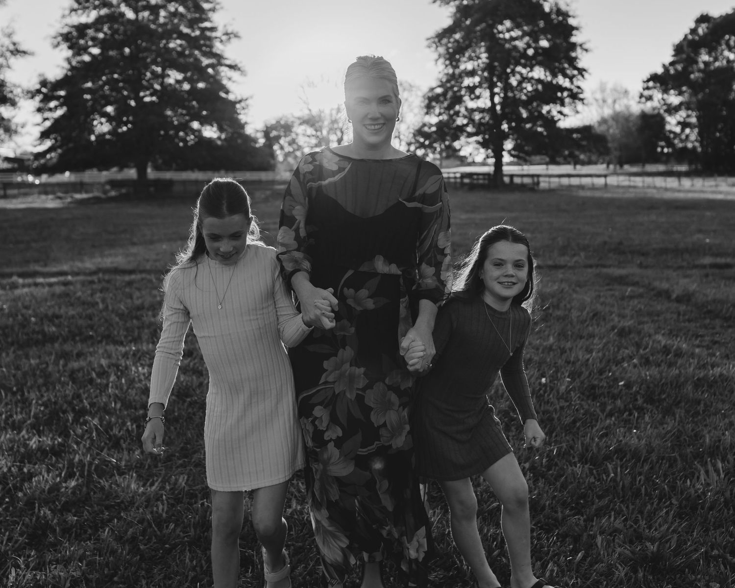 Black and white family portrait of mother with two daughters and dog in park at golden hour.