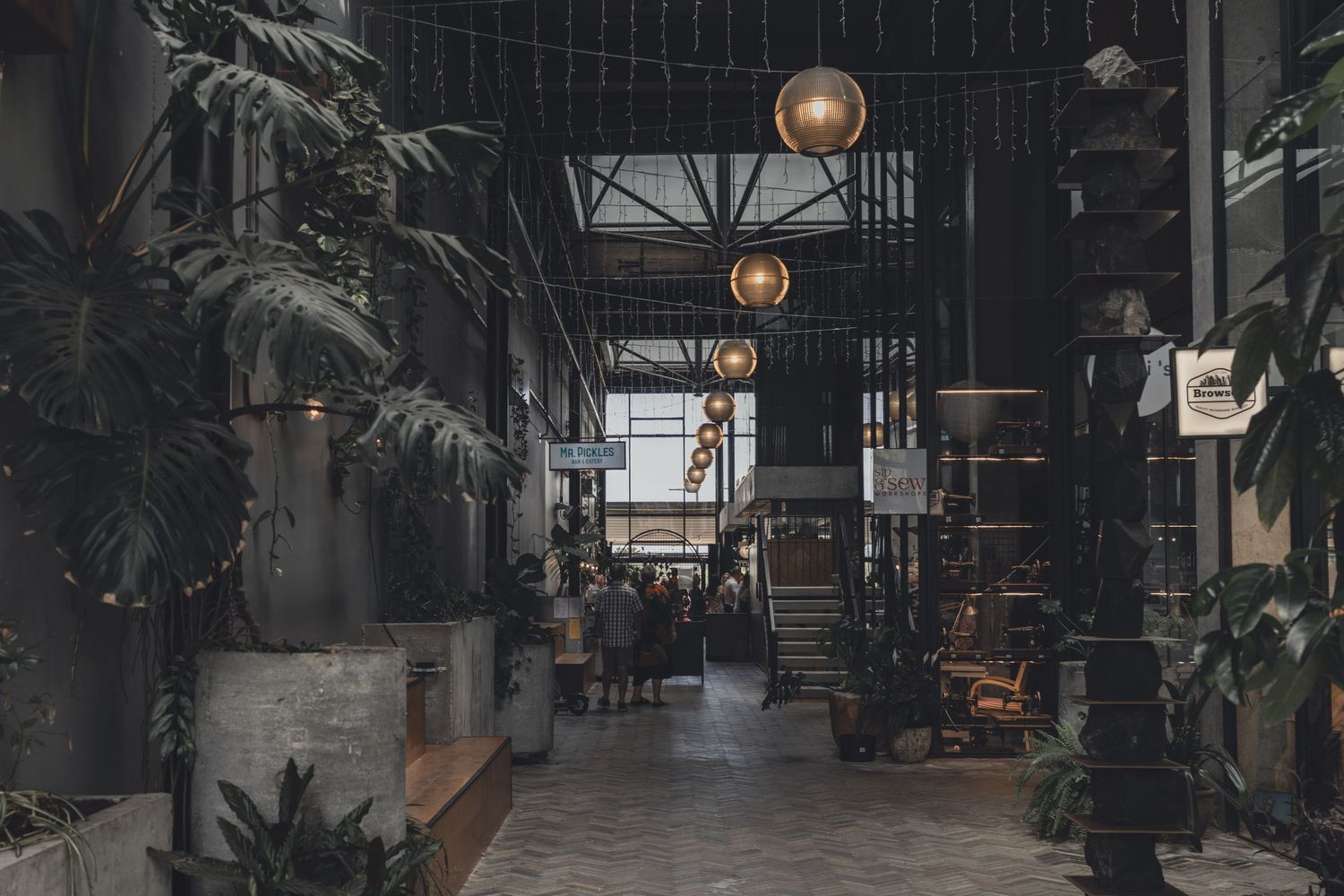 Stylish industrial venue interior with hanging globe lights and tropical plants.