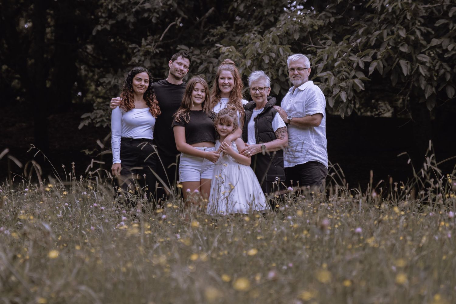 Extended family posing together in a golden wildflower field surrounded by trees.