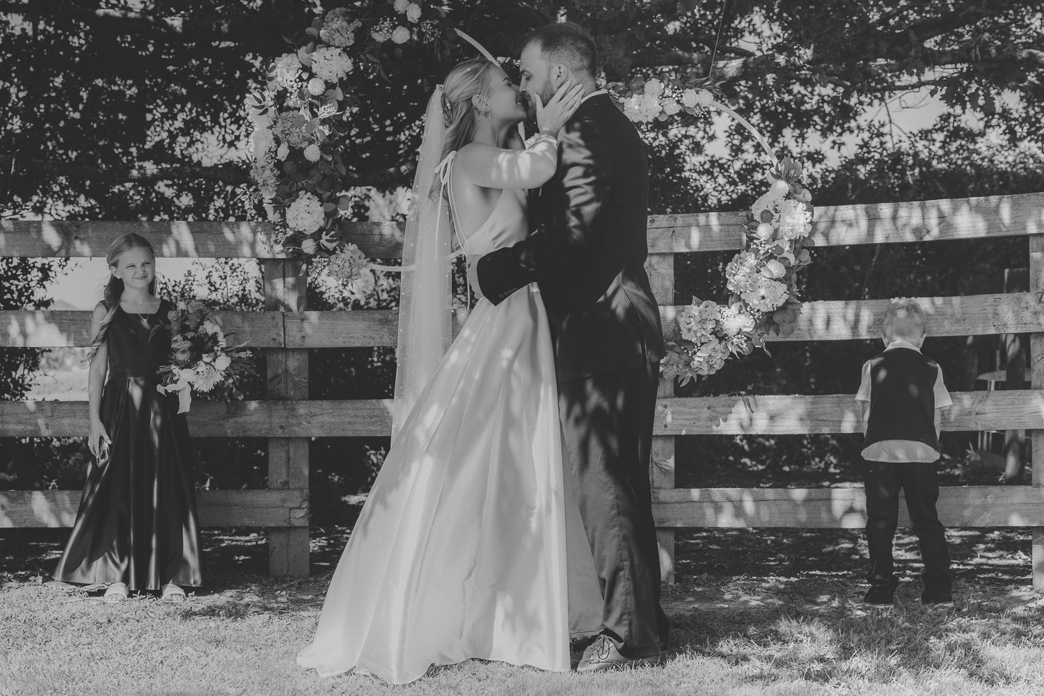 Black and white photo of a bride and groom sharing their first kiss at an outdoor wedding ceremony.