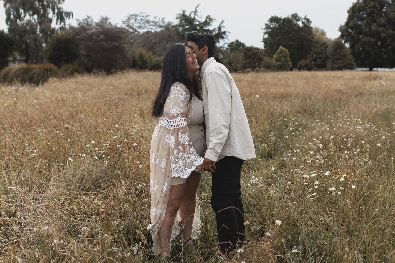 Couple sharing a kiss while holding hands in a sunlit wildflower meadow.