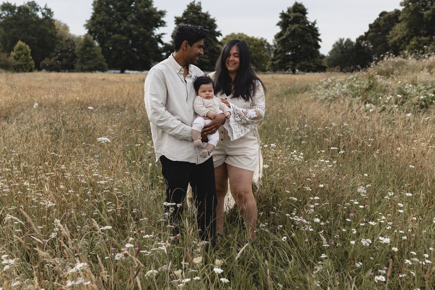 Happy family of three walking through wildflower meadow on overcast day.