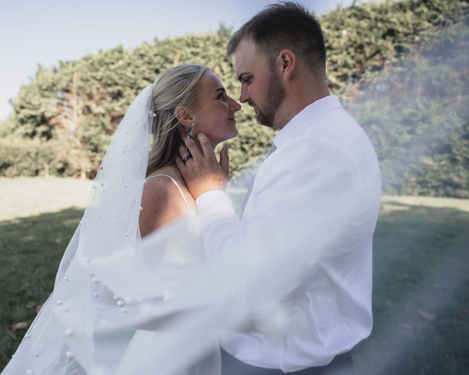 Bride and groom sharing a romantic moment outdoors, with wedding veil flowing, surrounded by lush greenery.