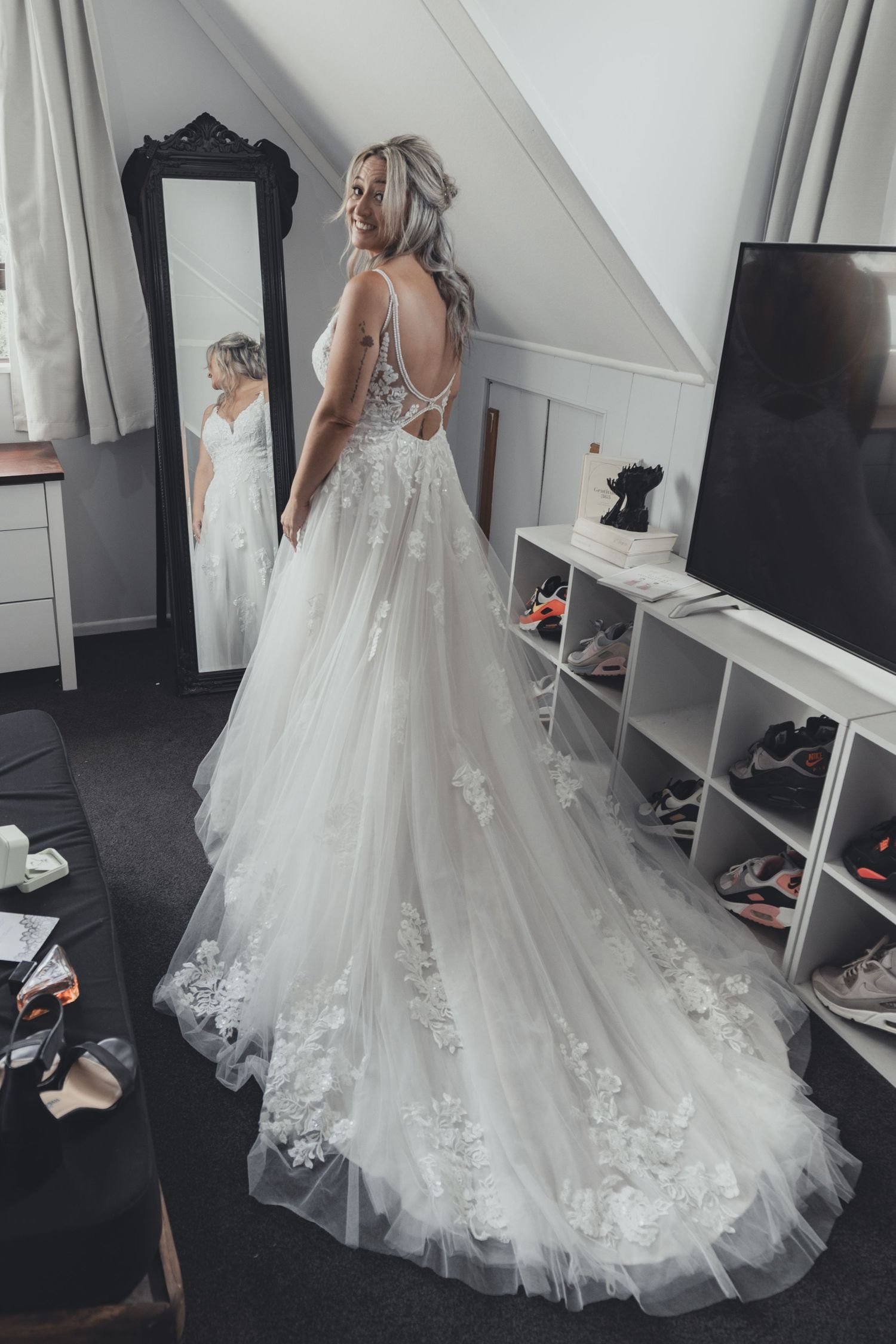 Bride in stunning lace A-line wedding dress smiling at mirror reflection in bedroom.