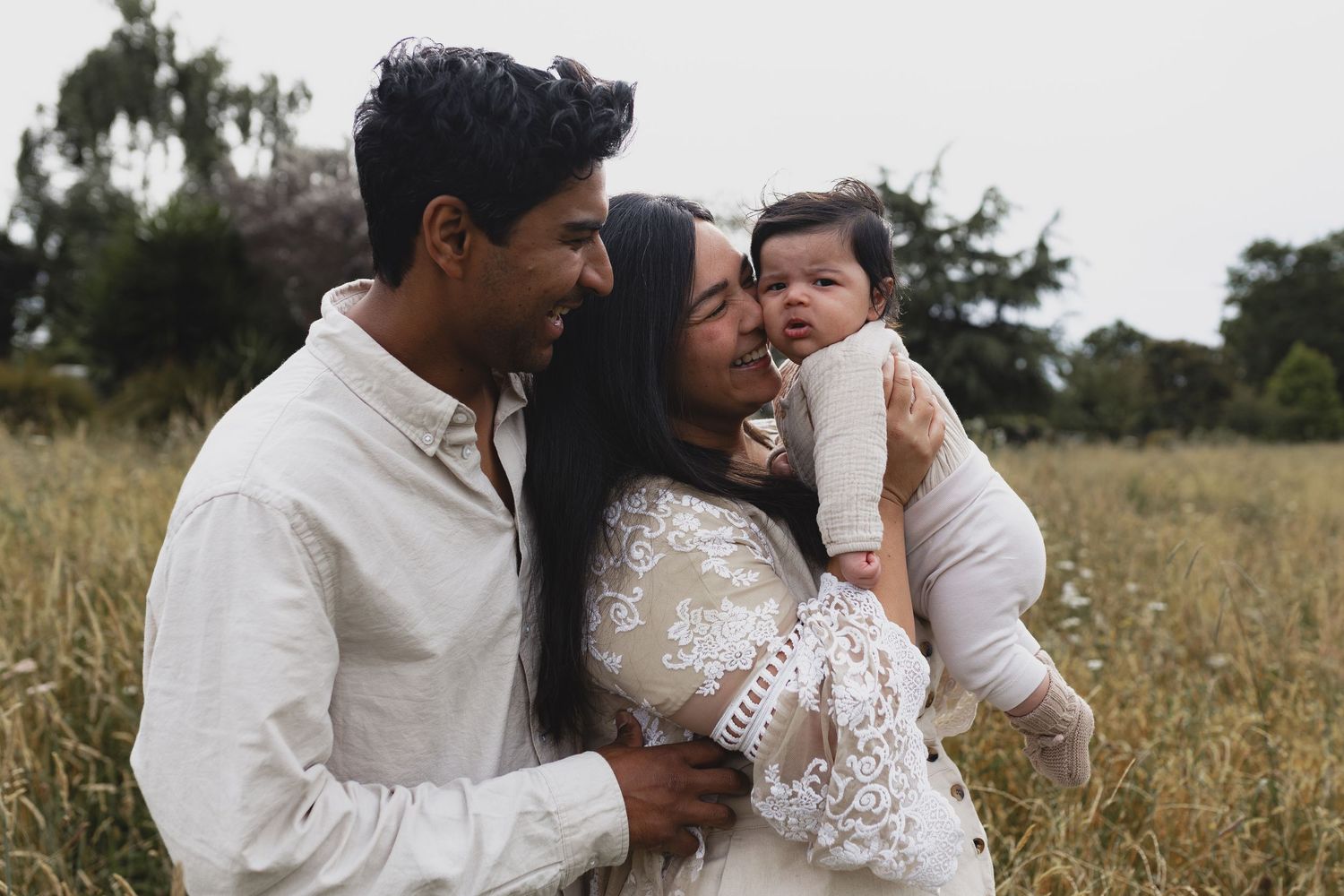 Young family with newborn baby sharing tender moment in golden meadow field.